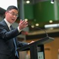 A man stands at a lectern with his hand raised.